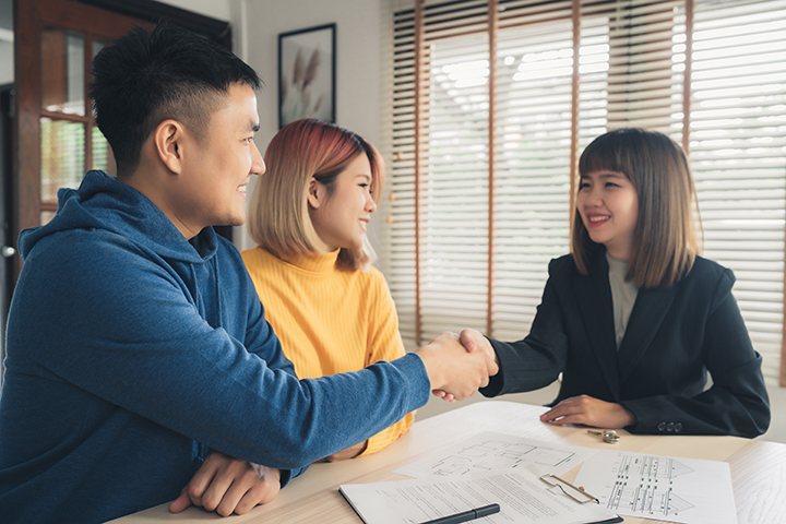 Asian couple shaking hands with a businesswoman while they finish signing paper work