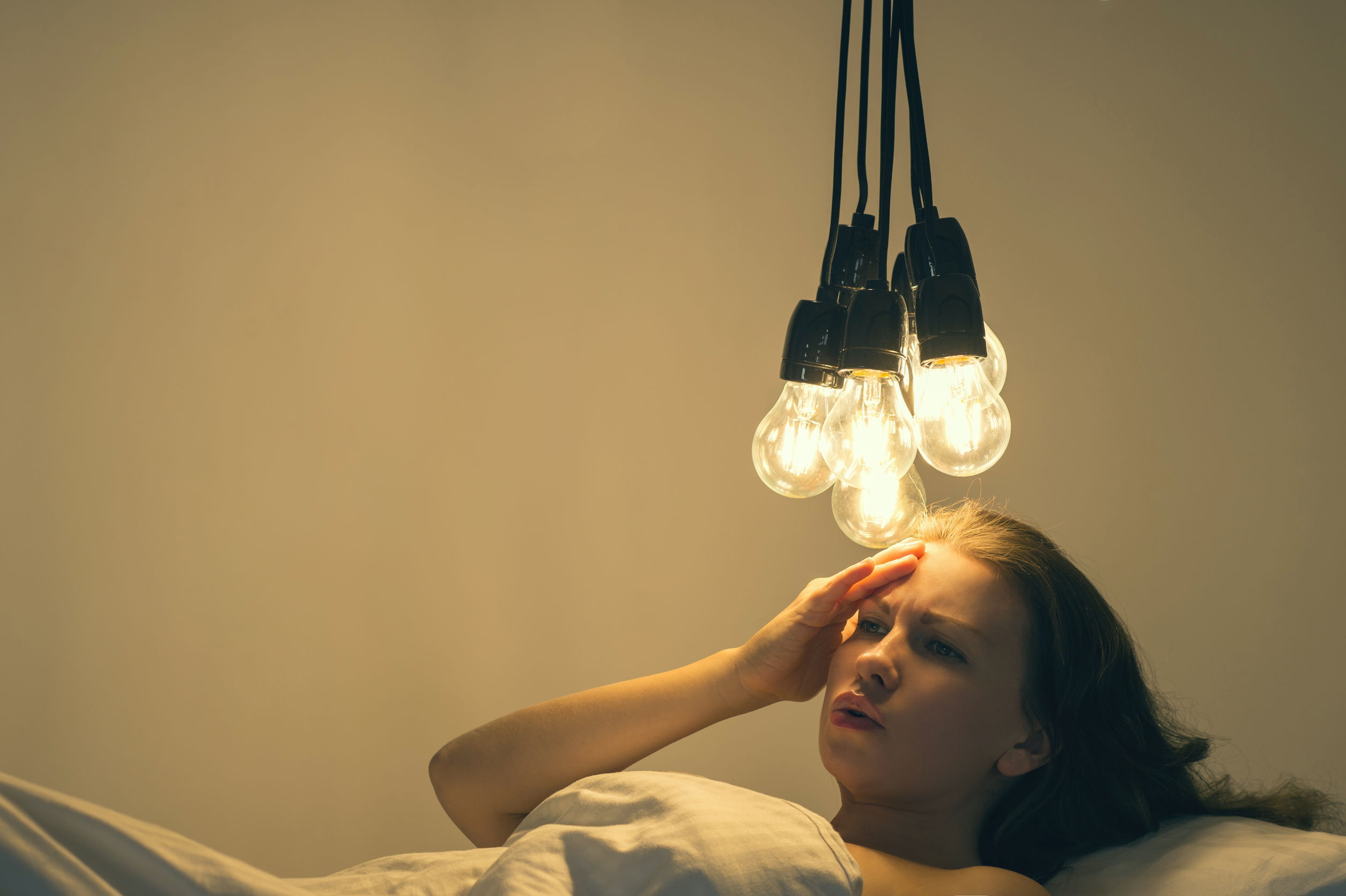 A girl cant sleep in a bed under a big light bulbs