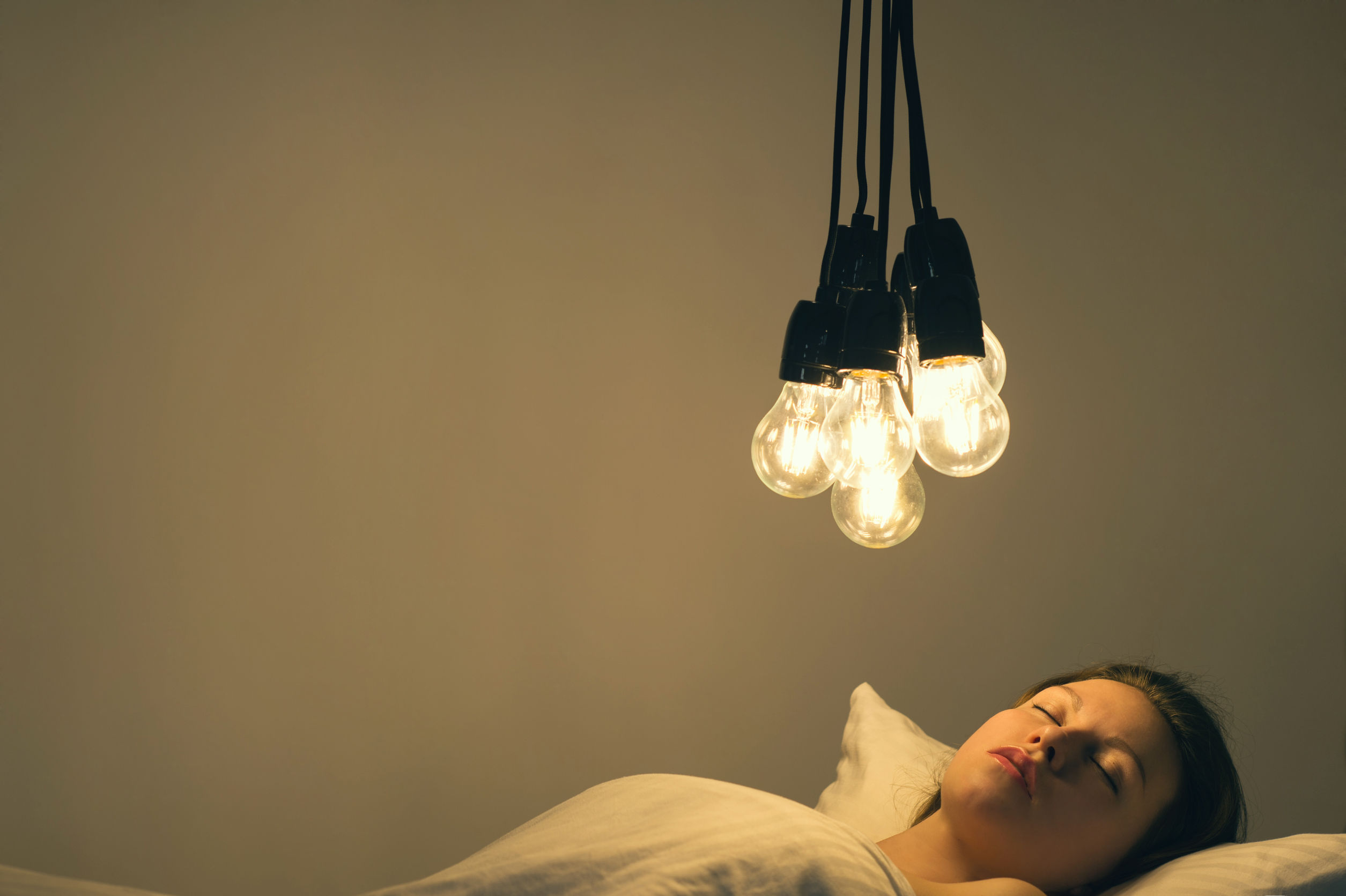 A girl lies in a bed under a big light bulbs