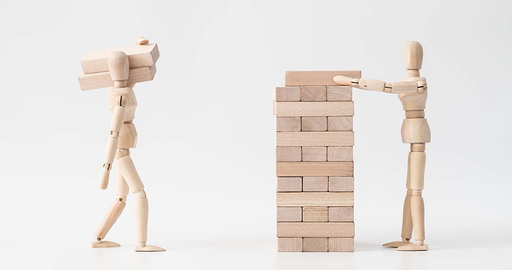 Two figures made of wood carrying wooden blocks to build a foundation for a business