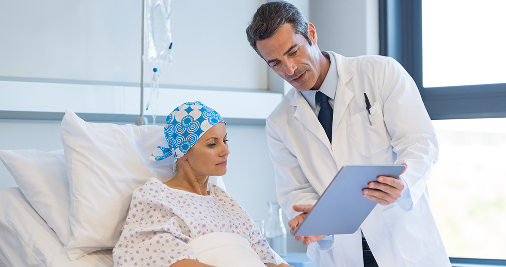 Médico varón hablando con una paciente de cáncer mujer hospitalizada que muestra los resultados de su prueba junto a su cama en una tableta