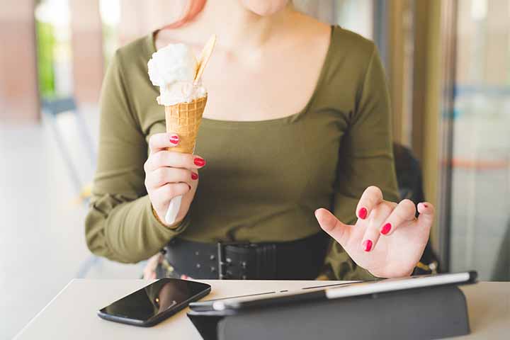 Woman holding an ice cream cone in one hand and writing on the tablet with the other