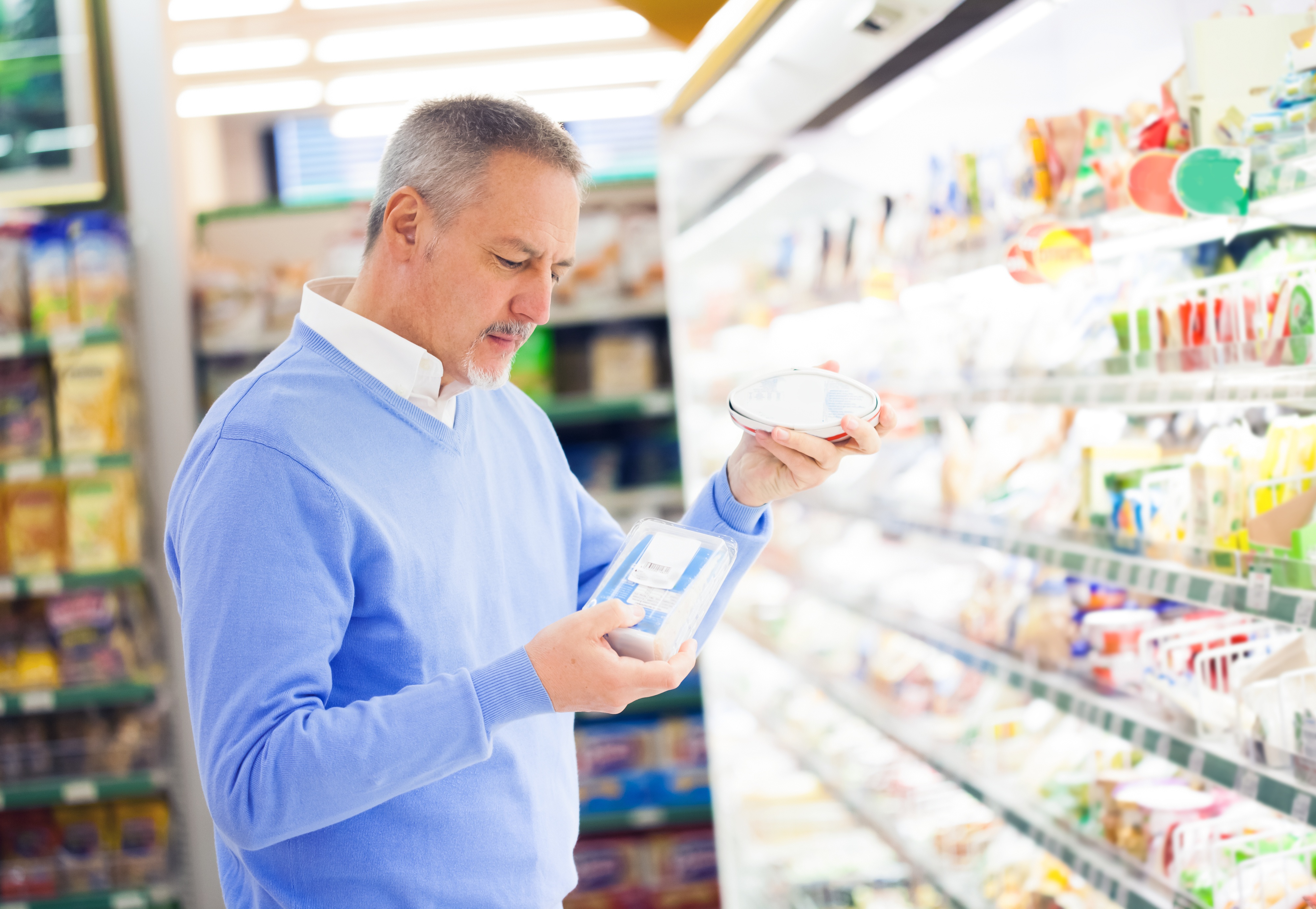 Hombre de mediana edad con un suéter azul mirando la sección de comida fría en la tienda de comestibles
