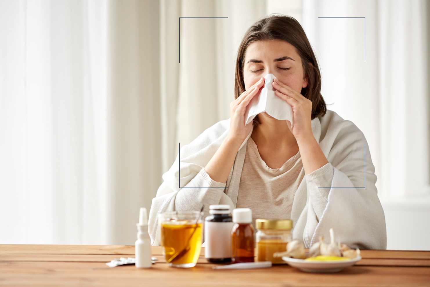 Mujer sentada en la mesa del comedor sonándose la nariz mientras está rodeada de medicamentos para el resfriado