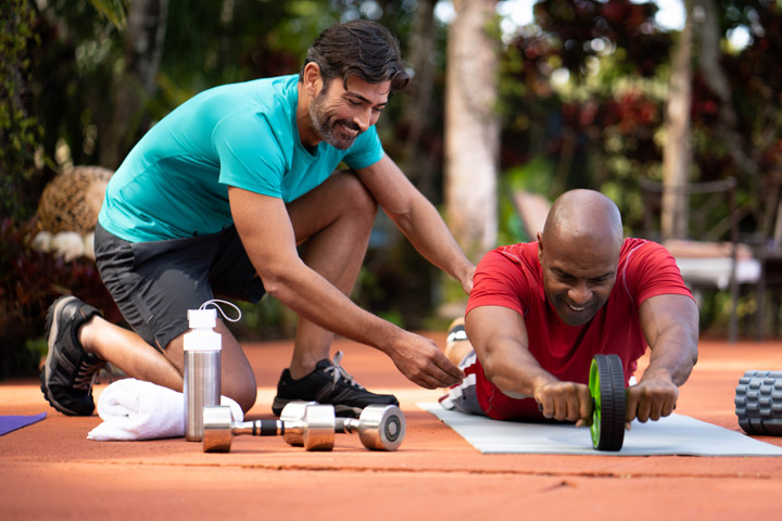 Male personal trainer training his male client how to properly do an ab workout outdoors on a yoga mat