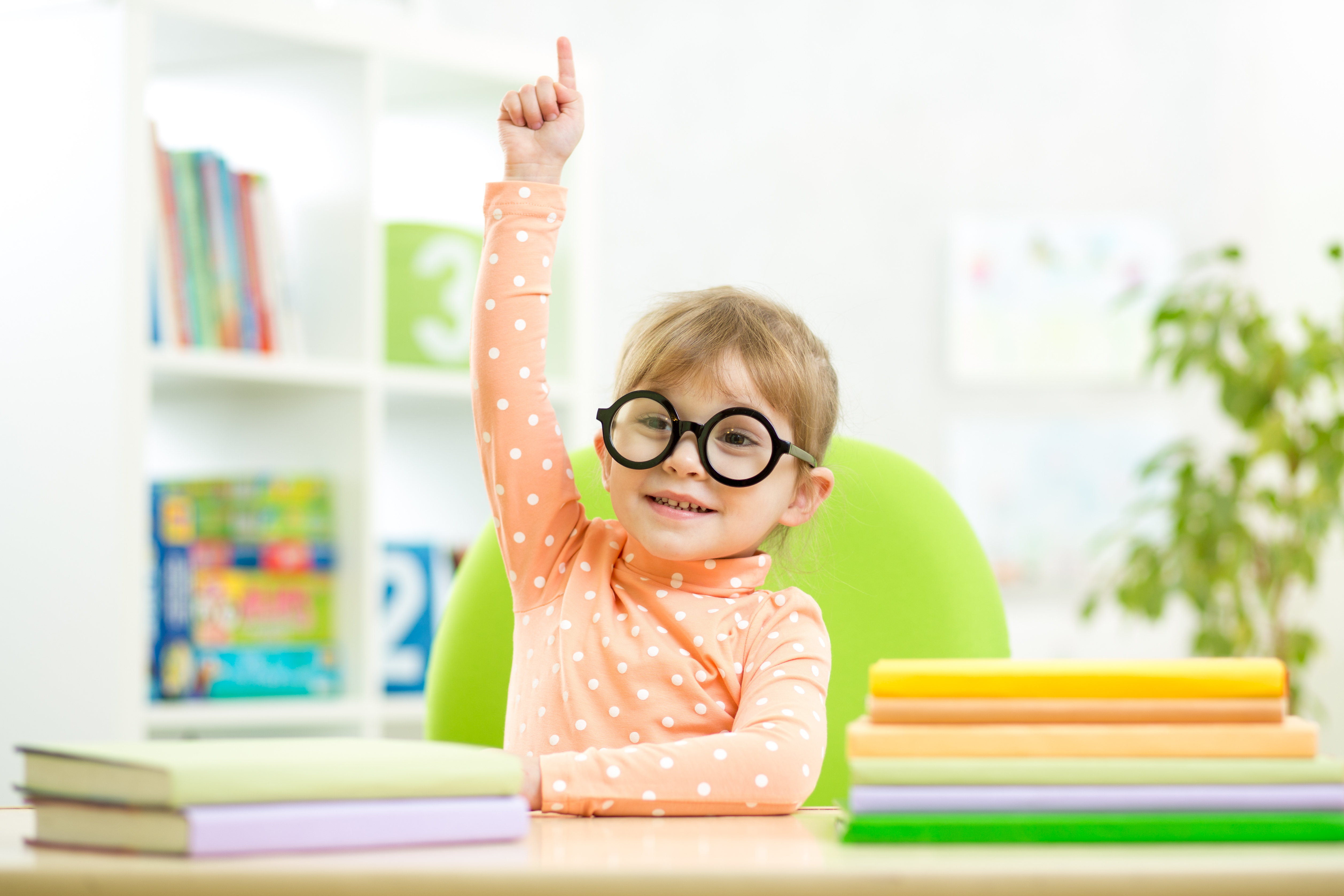 Little girl with glasses raising her hand in class