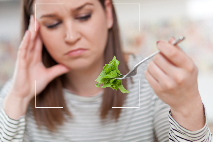 Woman eating a salad and looking sadly at her food