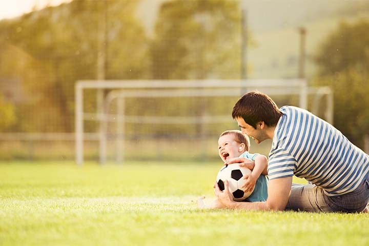 father teaching his toddler son how to play soccer on an empty soccer field