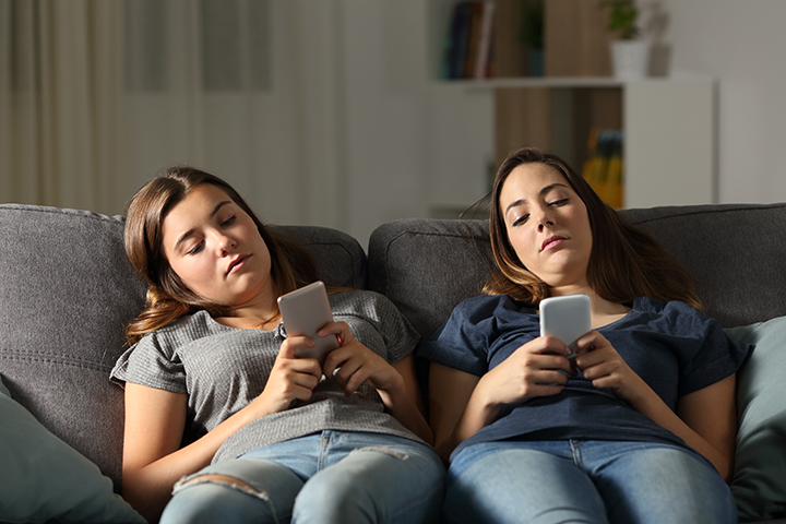 two teenage girls texting on couch