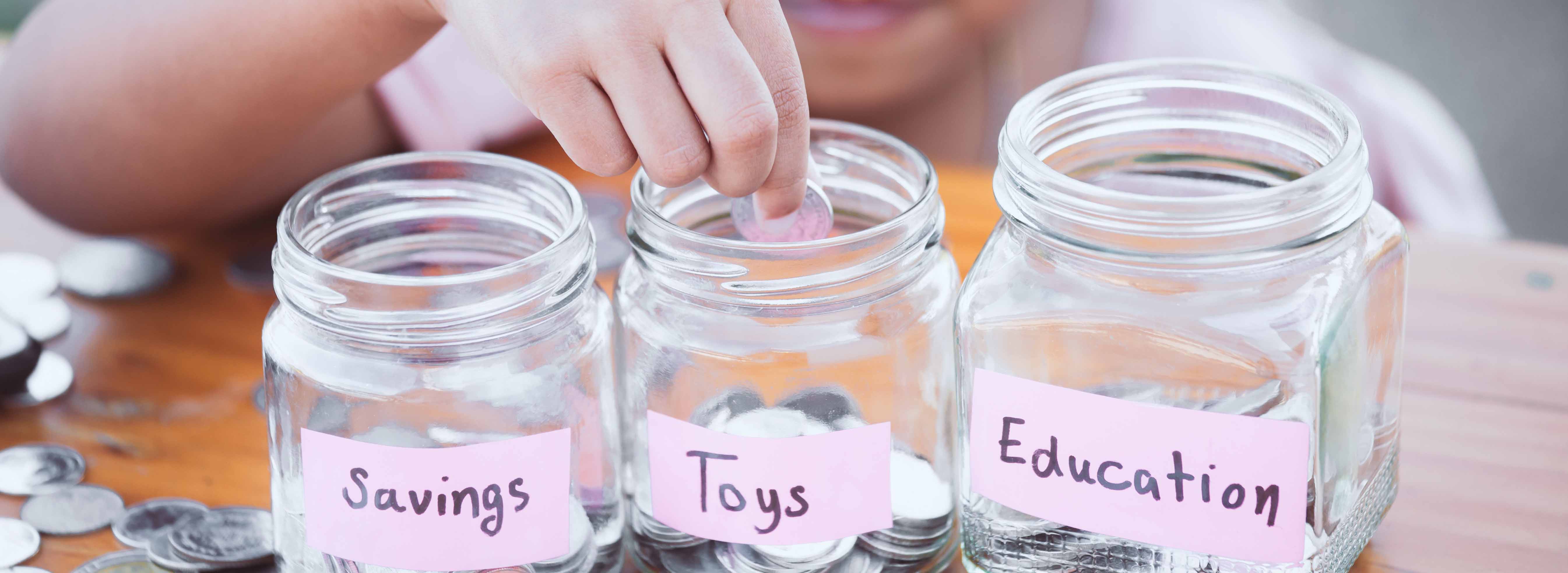 A young child placing coins in different piggy banks labeled toys